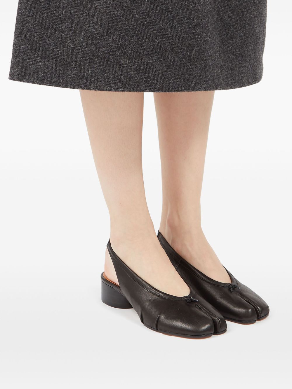 Black open-toe shoes worn with a gray skirt on a white background